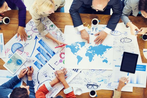 Internationales Business-Team analysiert Weltkarte und Diagramme als Grundlage für Übersetzung und Lokalisierung von Unternehmensinhalten.